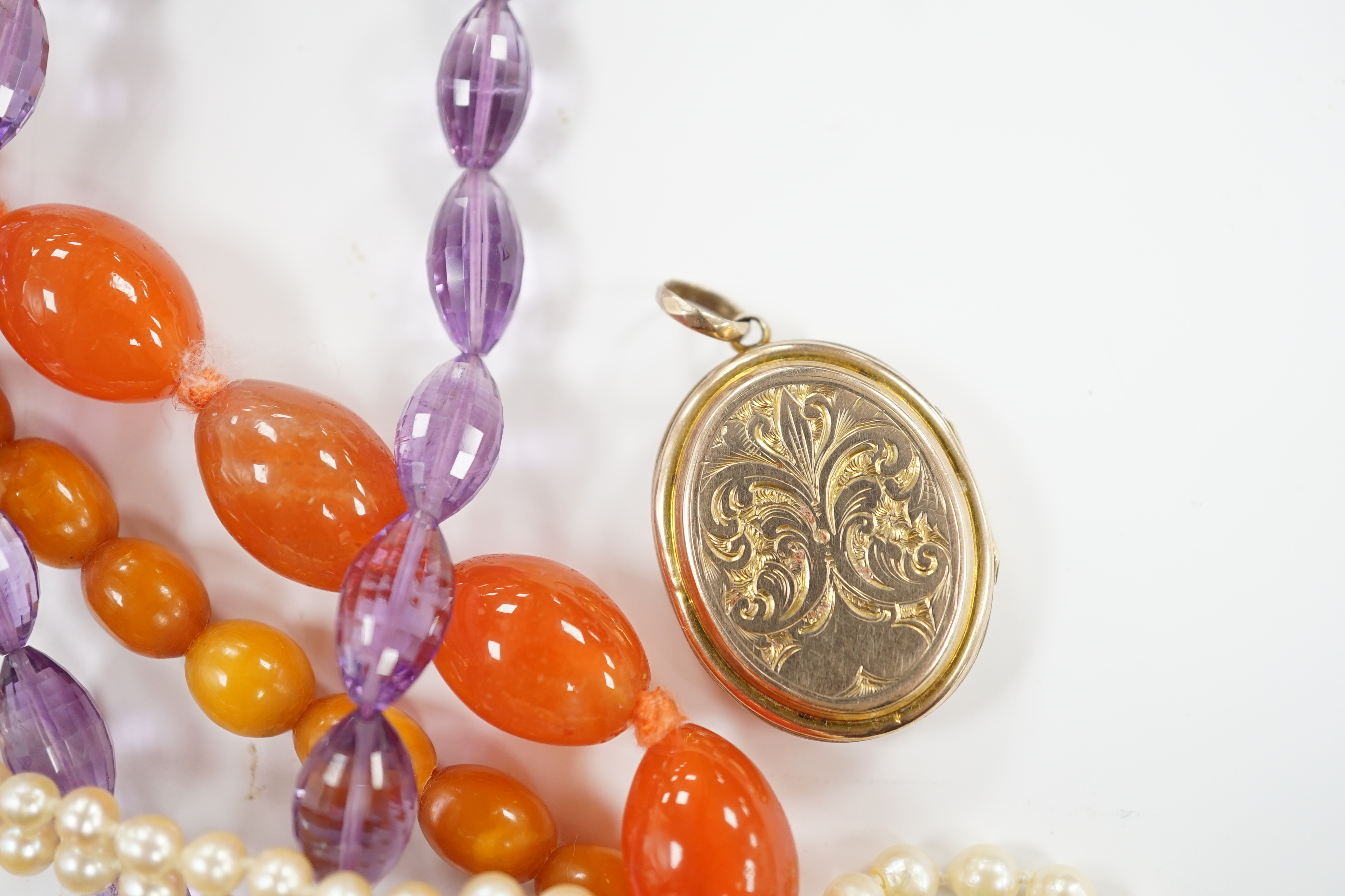 A gold plated oval locket and four assorted single strand necklaces including cultured pearl, amber, agate and amethyst.